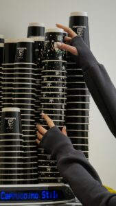 Hands arrange tall stack of branded paper coffee cups at a café, showcasing organization.