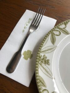 An elegant table setup featuring a fork on a branded napkin beside a decorative plate with leaf patterns.