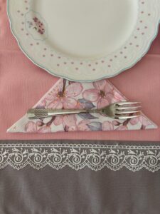 A detailed view of a classic porcelain plate with a floral napkin, a fork, on a lace-trimmed tablecloth.